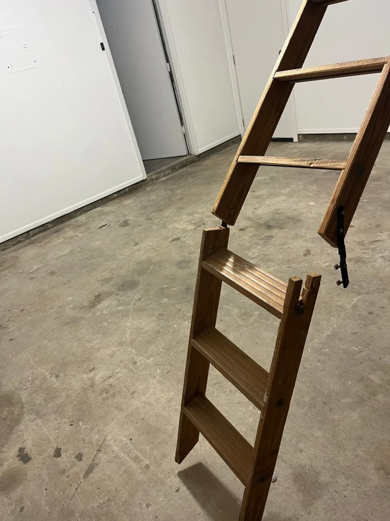 A broken wooden attic ladder with missing or damaged sections