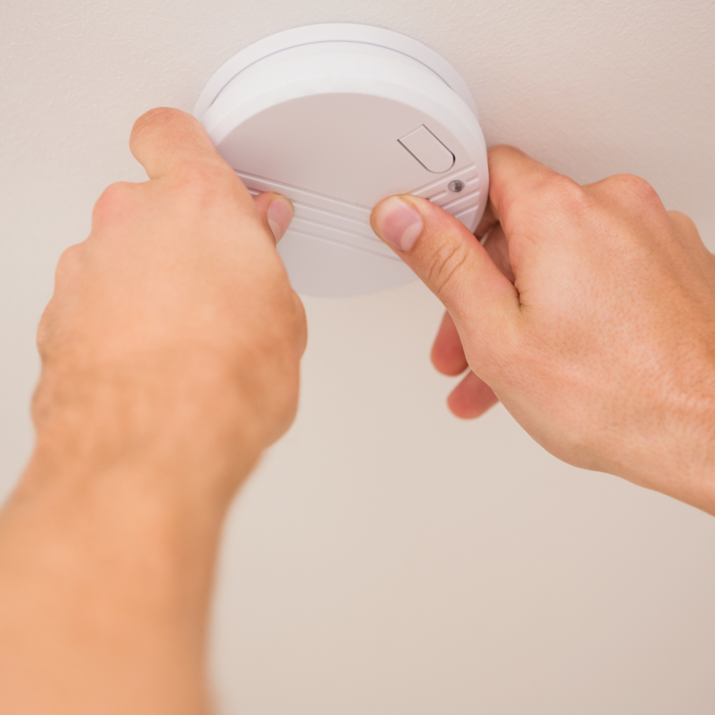 A person installing a smoke detector on a ceiling