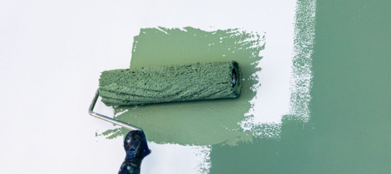 green paint roller rolling paint on a white wall