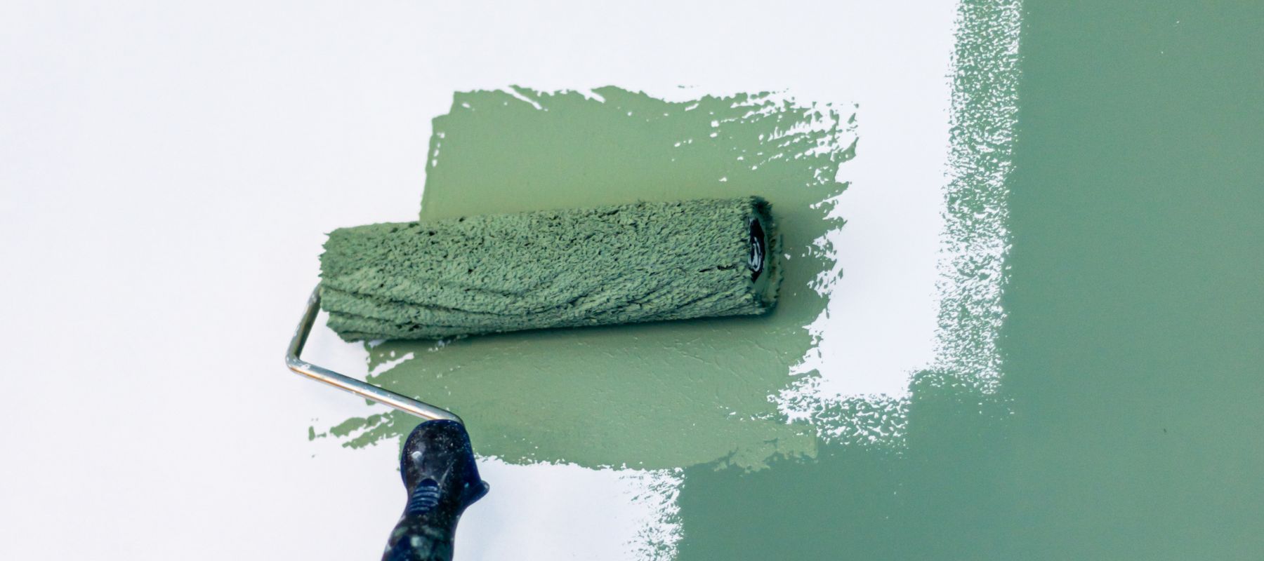 green paint roller rolling paint on a white wall