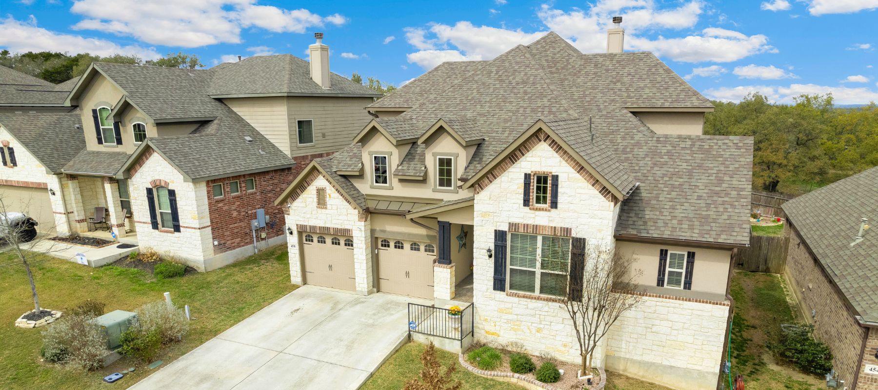 Two-story suburban home with stone and brick exterior, dual garage doors, and neatly landscaped front yard under a bright blue sky.