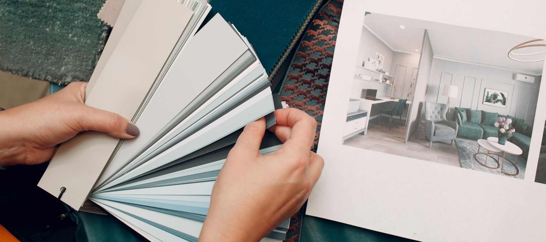 A person holds a fan of paint color swatches next to a printed interior design layout while planning home decor choices