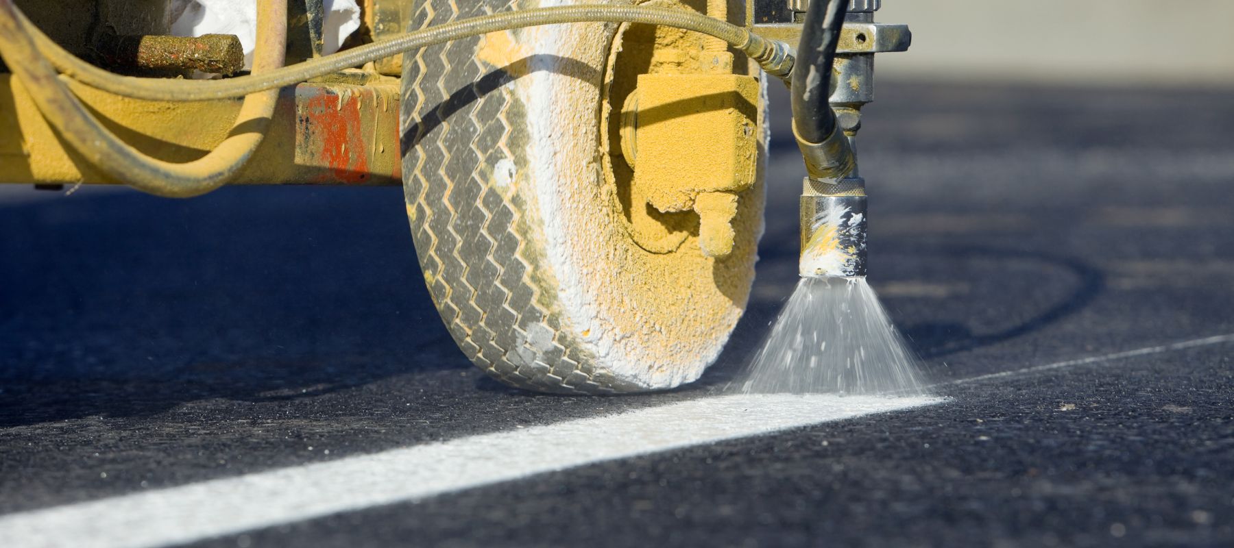 A line striping machine sprays white paint onto an asphalt parking lot surface