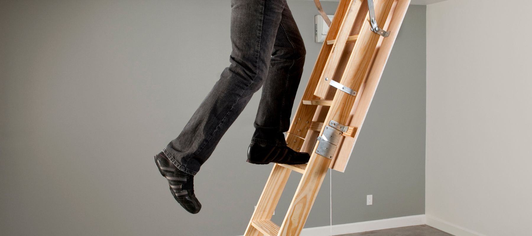 person wearing black jean pants and black shoes climbing up an attic ladder
